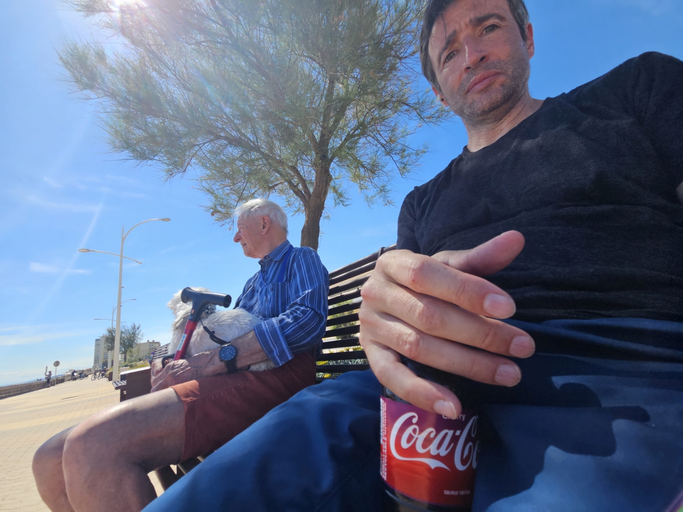 Angel und André (90 Jahre) auf einer Bank in Valras-Plage, mit kleinem weißen Hund